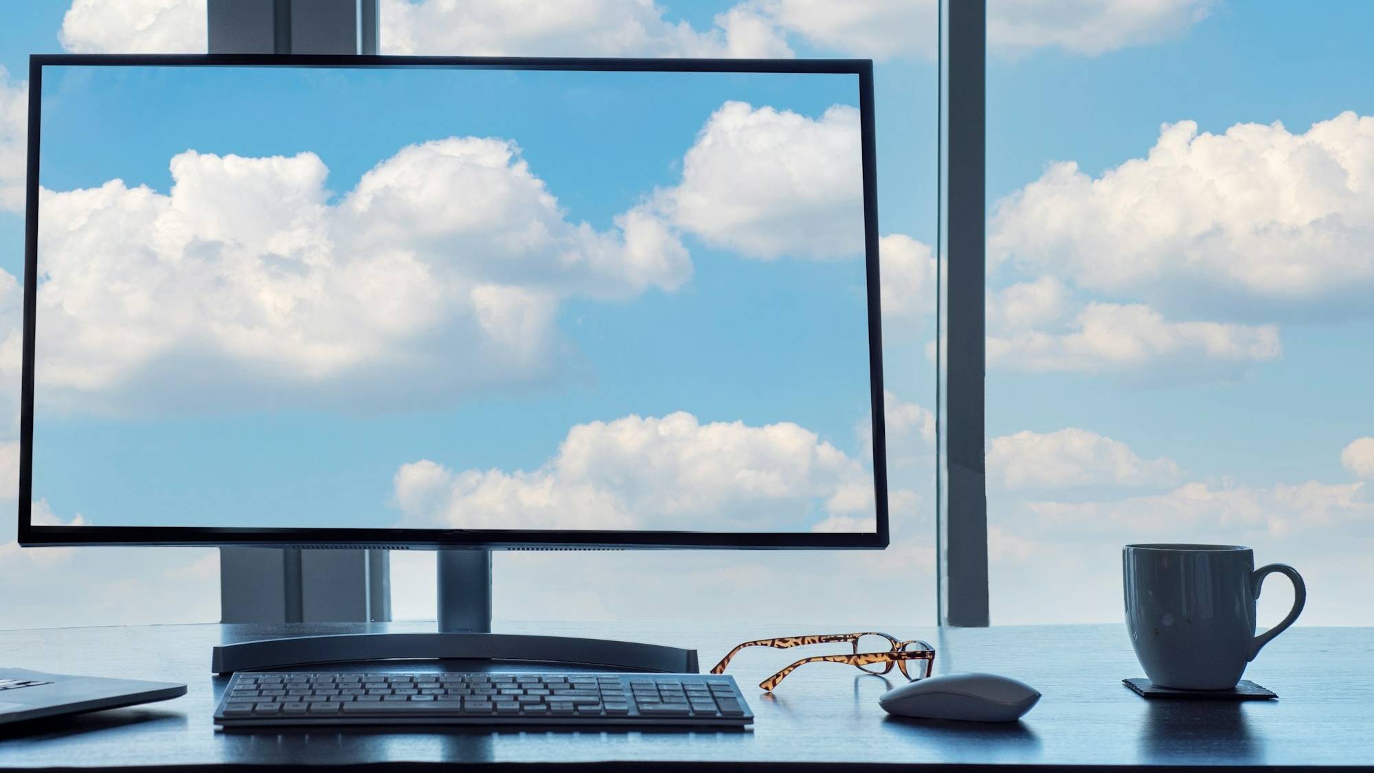 Conceptual cloud computing desk with computer, keyboard, mouse, eyeglasses and coffee.