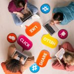 Overview of four young contemporary friends using mobile gadgets on the floor