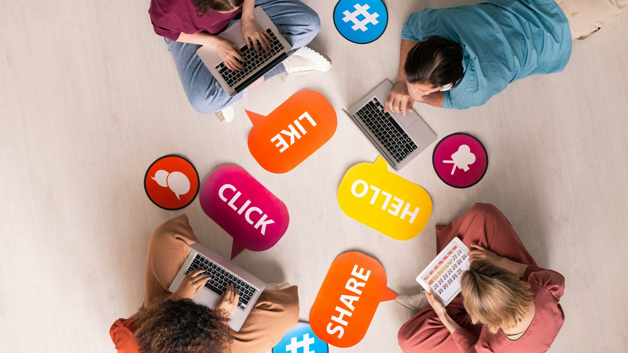 Overview of four young contemporary friends using mobile gadgets on the floor