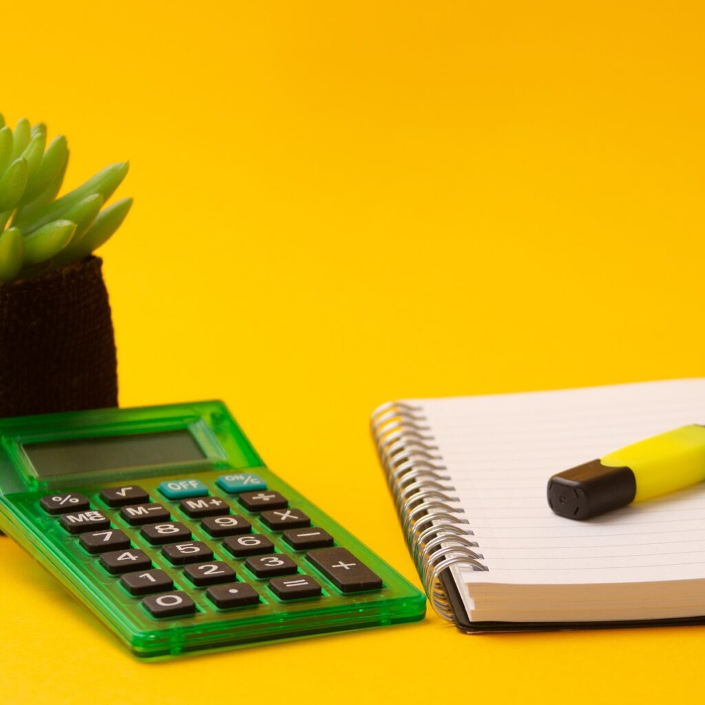 Selective focus shot of highlighter on a journal, calculator, and a plant on a yellow background