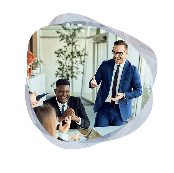 A Digital Enablement specialist from the Mint Group, wearing glasses, standing, smiling and engaging a room full of happy stakeholders.