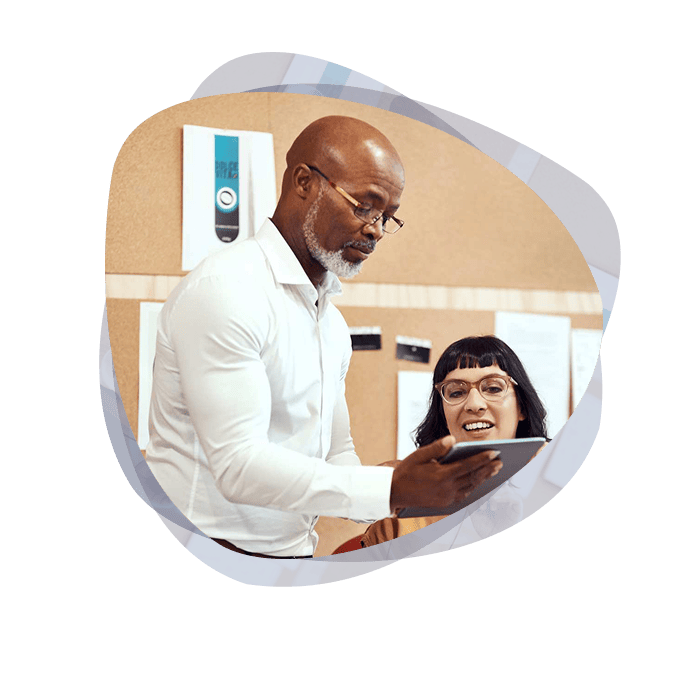 A Digital Transformation specialist, wearing a white shirt and blue pants, shows an employee training academy material on his tablet while standing next to the employee who is seated at her station.