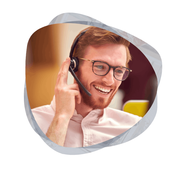Close-up of a smiling male customer service representative with red hair and glasses, wearing a headset and adjusting his microphone.