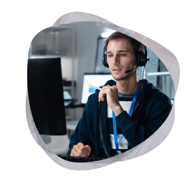 An IT professional wearing a headset and holding a pen while actively working on custom Teams application development at his computer.