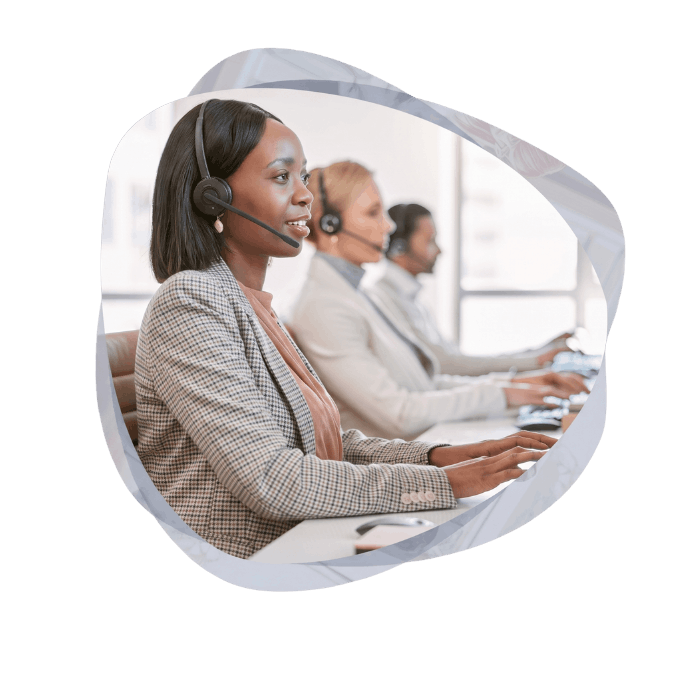 Side profile of a focused female call center agent wearing a headset and typing on a keyboard, with other agents working in the background.