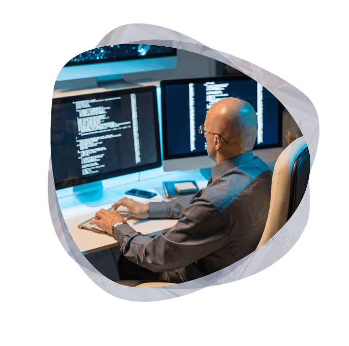 A programmer writing code on multiple monitors, building custom software systems to modernize legacy processes.