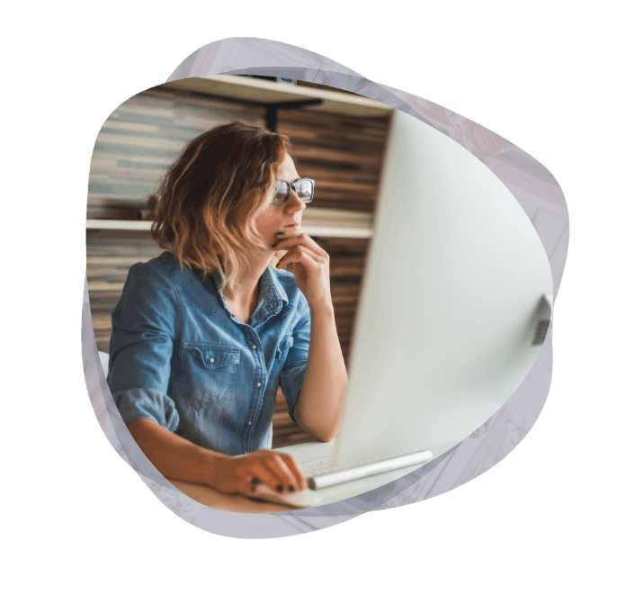 A professional woman with glasses thoughtfully looking at her desktop monitor to understand what are intranet development solutions for her business.