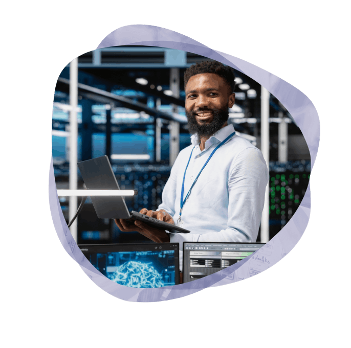 A smiling man with a beard holding a laptop in a server environment that runs on Microsoft Azure cloud services.