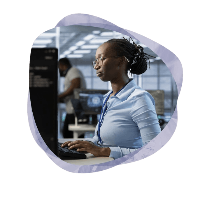 A focused professional woman with braided hair and glasses types on a keyboard at her desk in a modern Azure data centre environment.