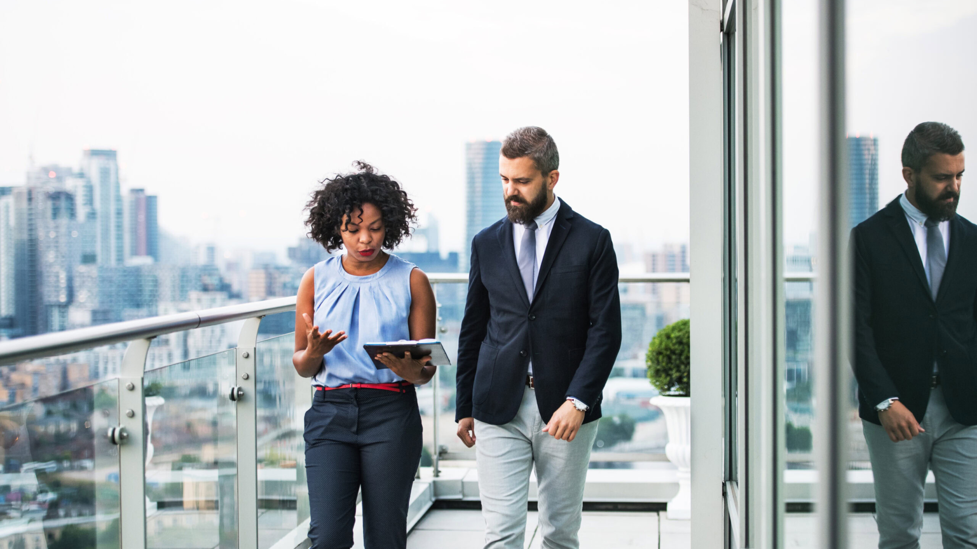 A portrait of businesspeople walking against London rooftop view, discussing something.