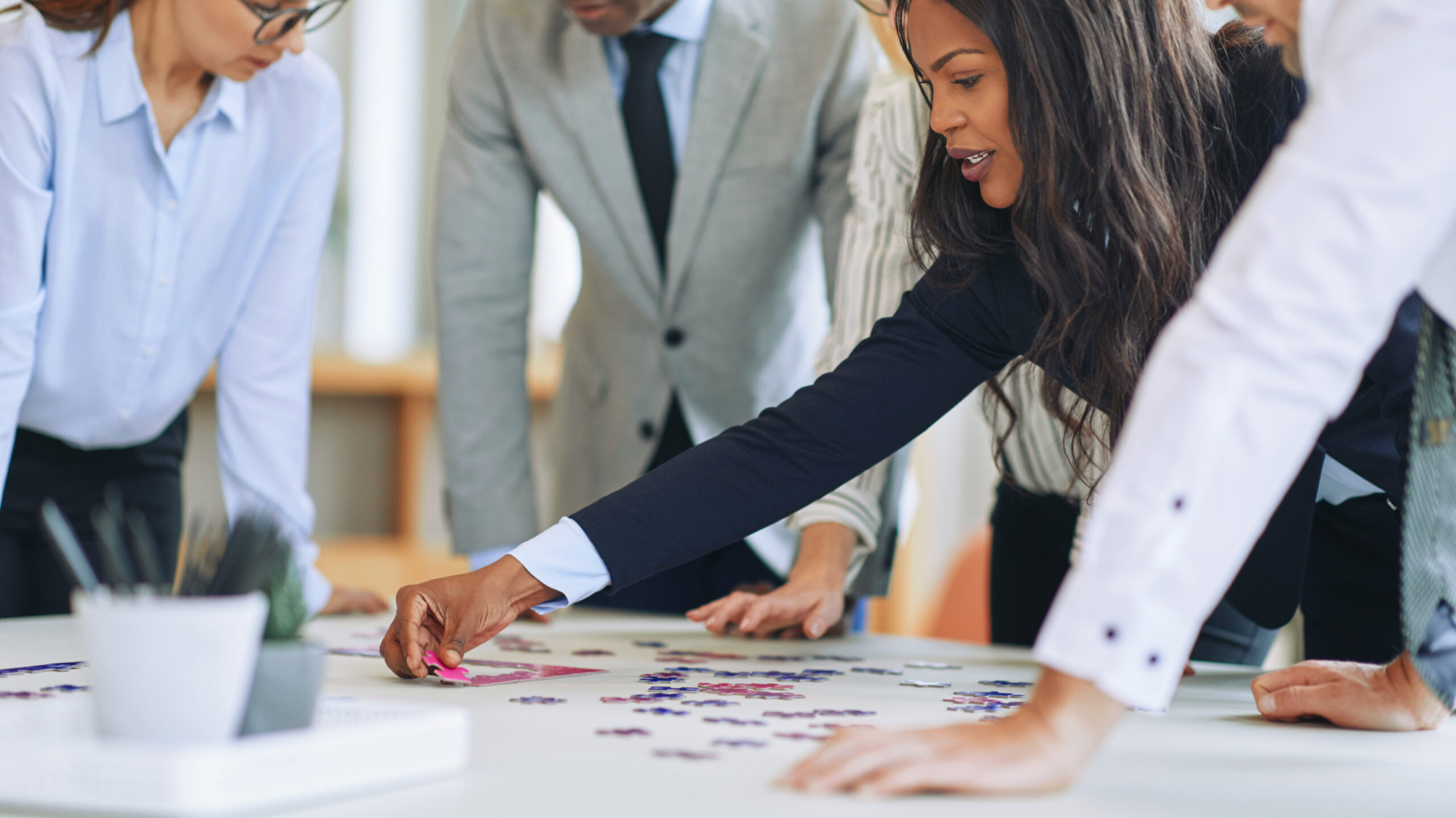 Diverse group of businesspeople trying to solve a jigsaw puzzle together around a boardroom table in an office