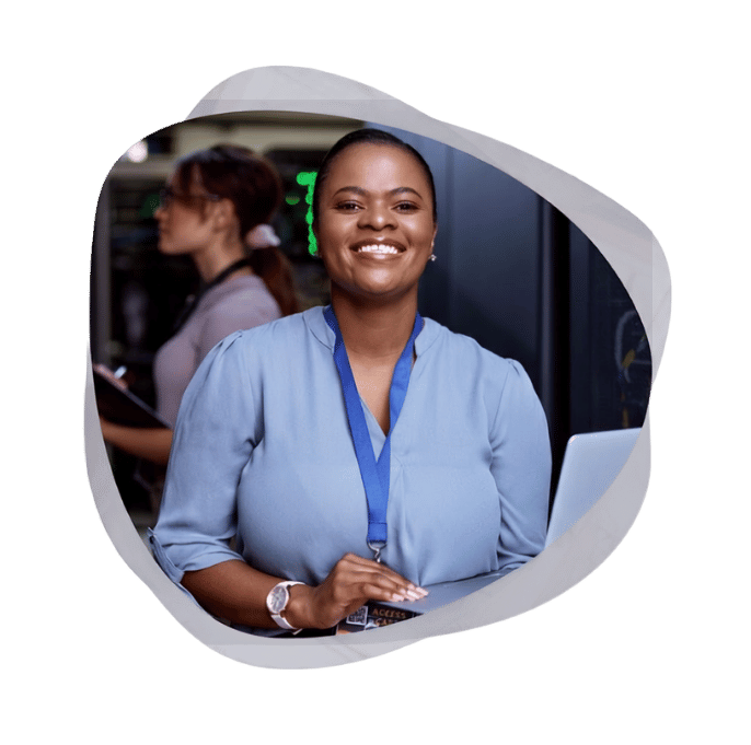 Alt text: A smiling Mint Group engineer holding a laptop in a data centre, supporting a client's Microsoft managed services environment while a colleague works in the background.